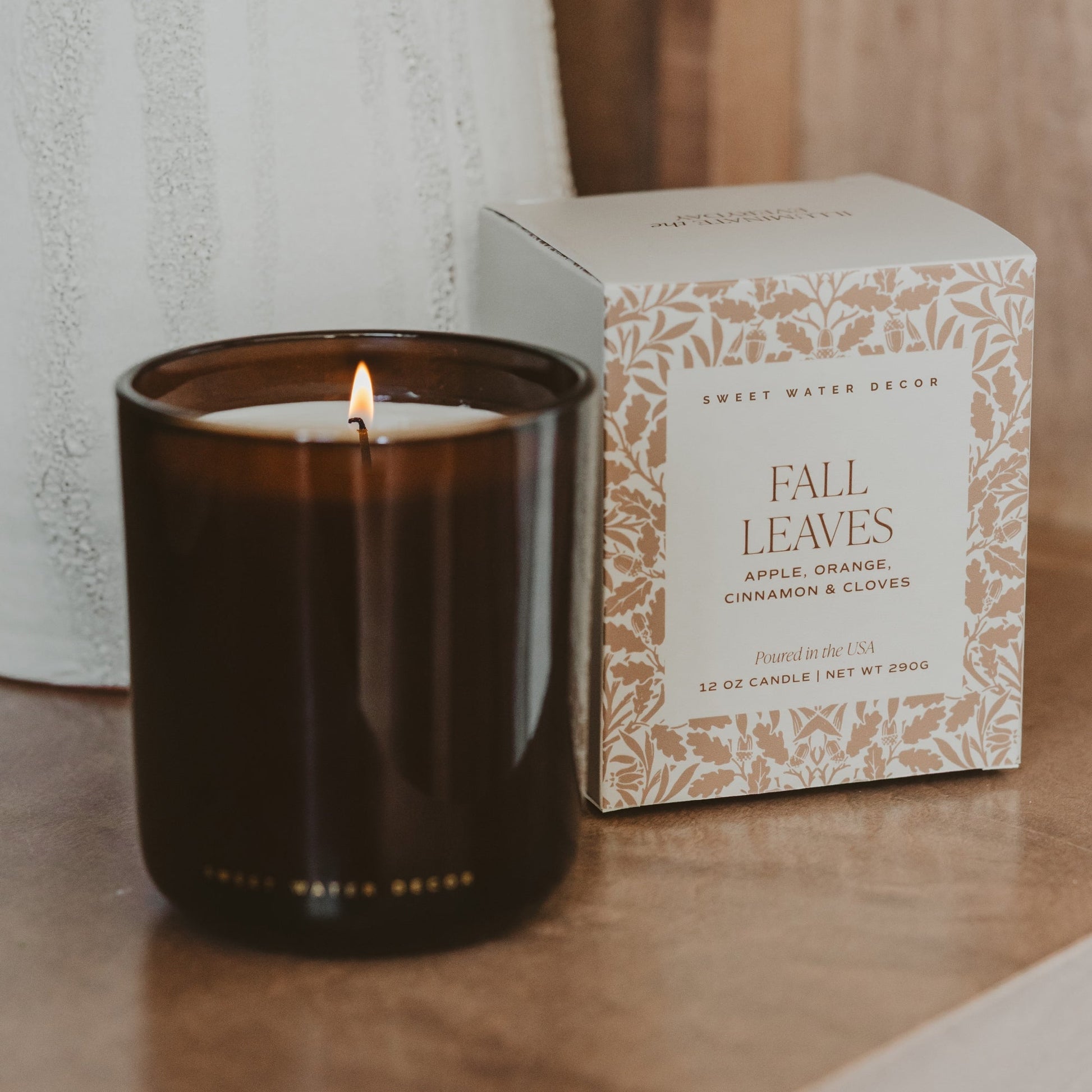Lit Fall Leaves candle in amber glass beside its botanical print box