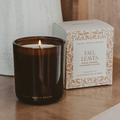 Lit Fall Leaves candle in amber glass beside its botanical print box