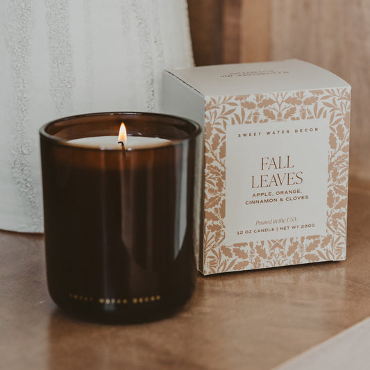 Lit Fall Leaves candle in amber glass beside its botanical print box