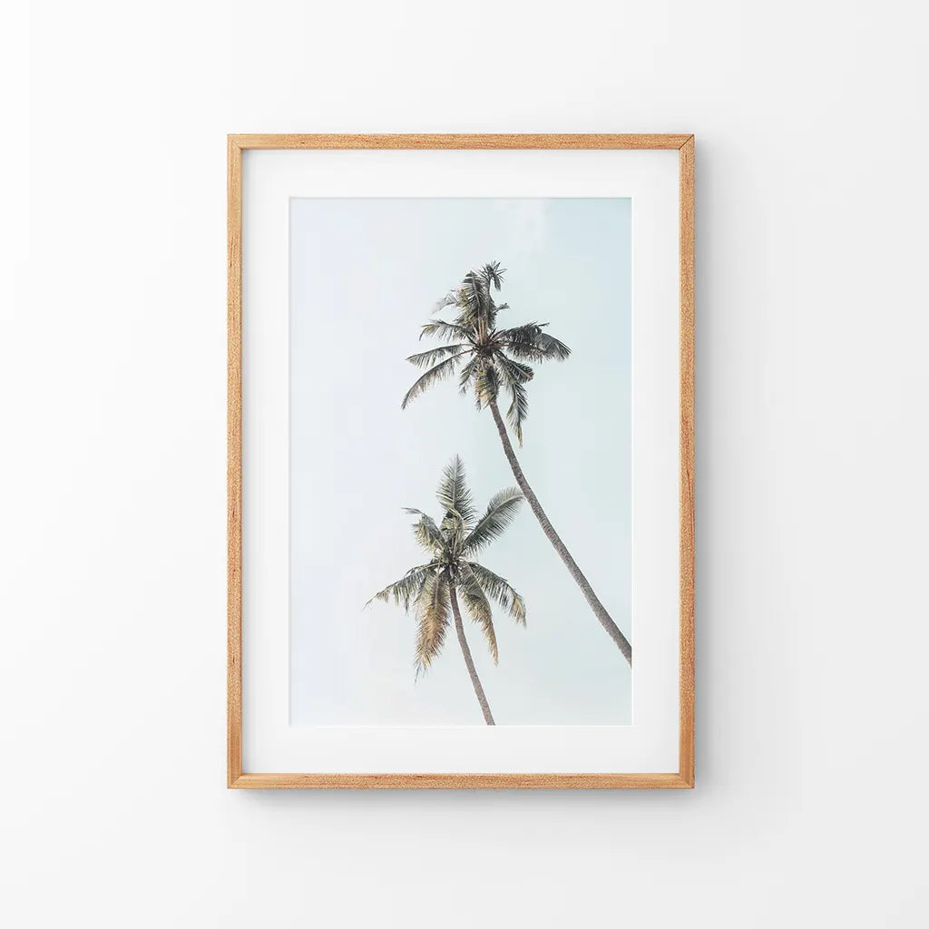 Two tall palm trees against a pale sky in a thin wood frame with mat