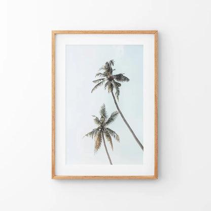 Two tall palm trees against a pale sky in a thin wood frame with mat