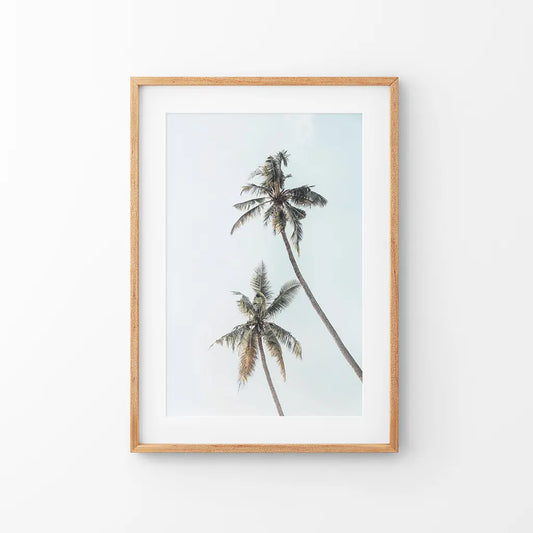 Two tall palm trees against a pale sky in a thin wood frame with mat
