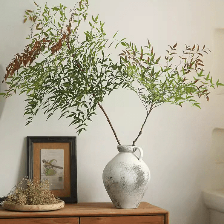 White one-handle pottery vase with airy greenery on a wooden sideboard