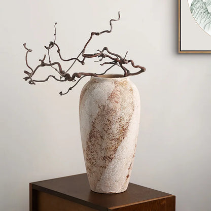 Tall weathered clay jar with a sculptural branch on a wooden stool
