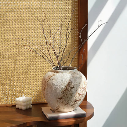 Round weathered clay jar with dried branches on a wood side table