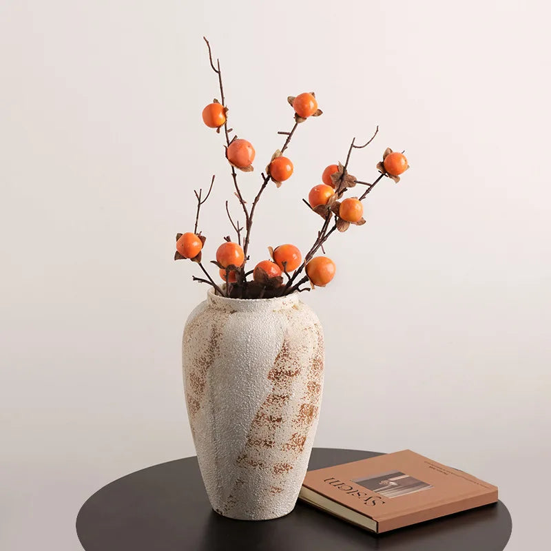 Tall weathered pottery jar holding persimmon stems on a dark table