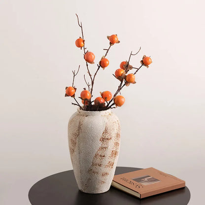 Tall weathered pottery jar holding persimmon stems on a dark table