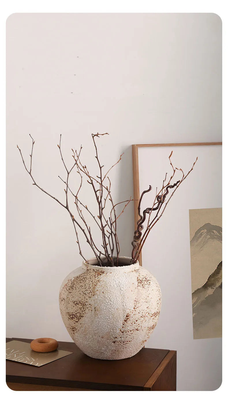 Round weathered clay jar with bare branches beside framed art