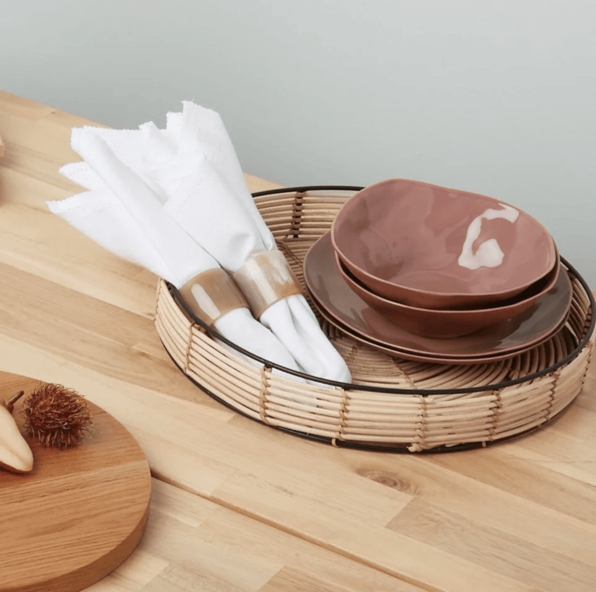 Cloth napkins in wooden rings on a cane tray beside stoneware