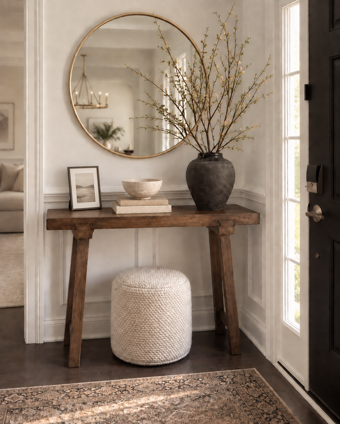 Our foyer console with a round brass mirror, branch vase, picture frame, books and a woven pouf
